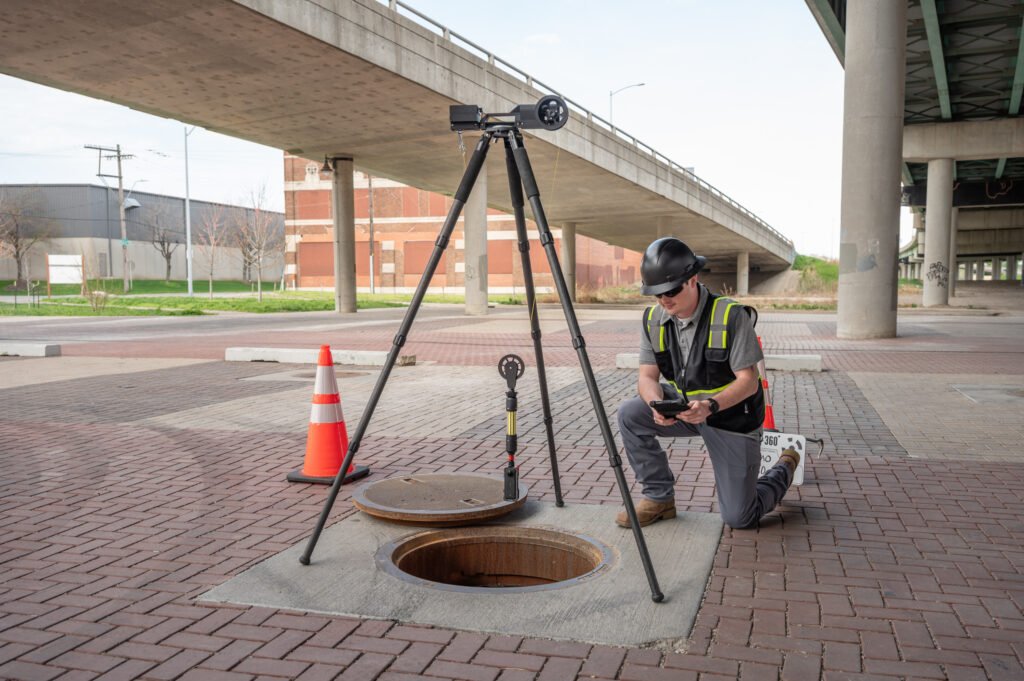 Operator kneeling beside the TREKK360 tripod during a manhole inspection