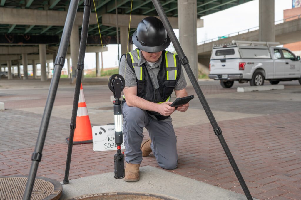 Operator using a tablet beside the TREKK360 tripod at an open manhole